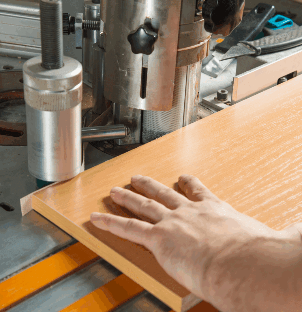 Hand guiding wood through industrial cutting machine.